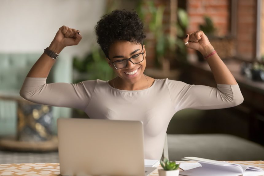 An excited female student looking at her laptop and punching the air.