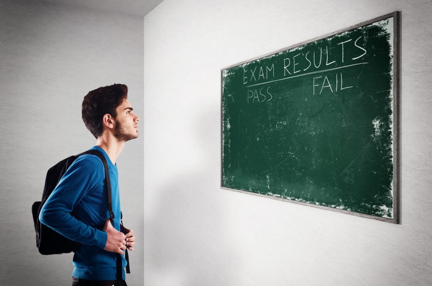 Male student looking at an exam results board which states pass or fail.