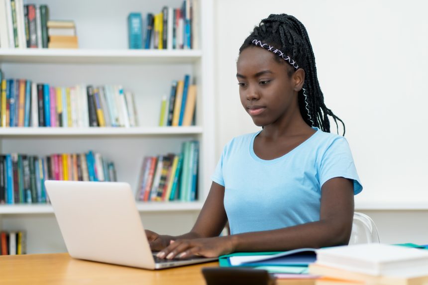 A female student writing her personal statement on her laptop in the school library.