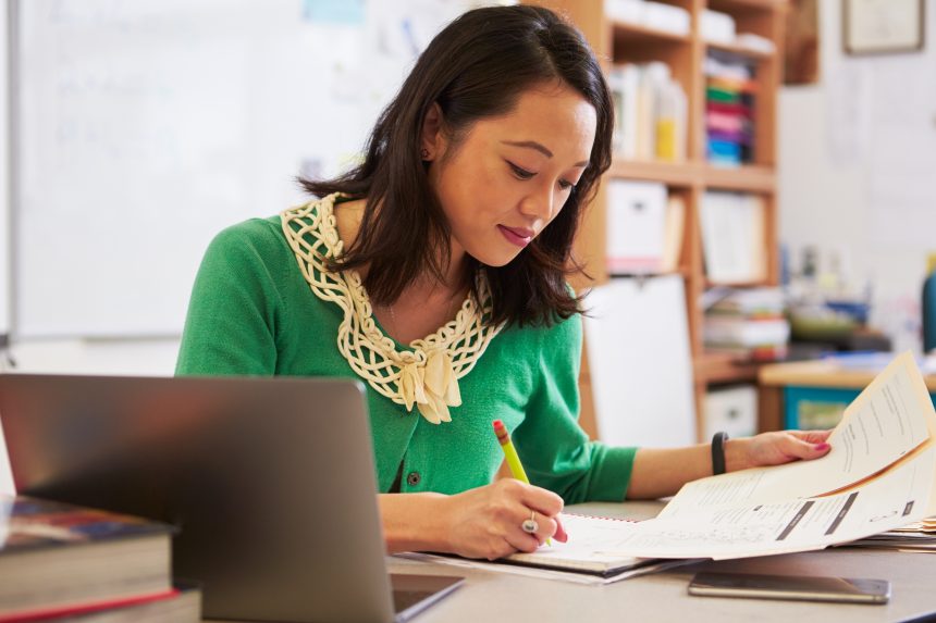 A female teacher sat at her desk and marking a piece of work.