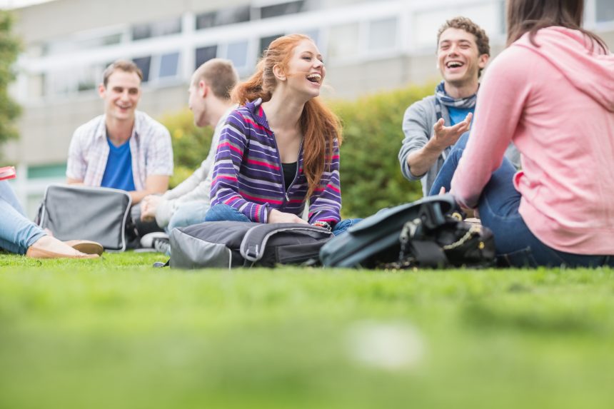 A group of students sitting on the grass outside their college campus.