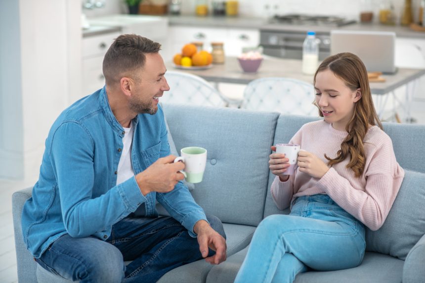 Dad and daughter sitting on a couch chatting.