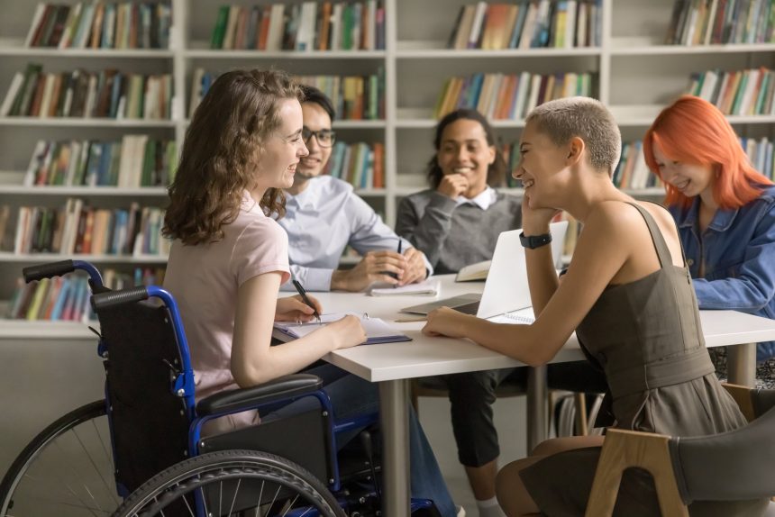 A female university student sitting in a wheelchair and chatting with friends.