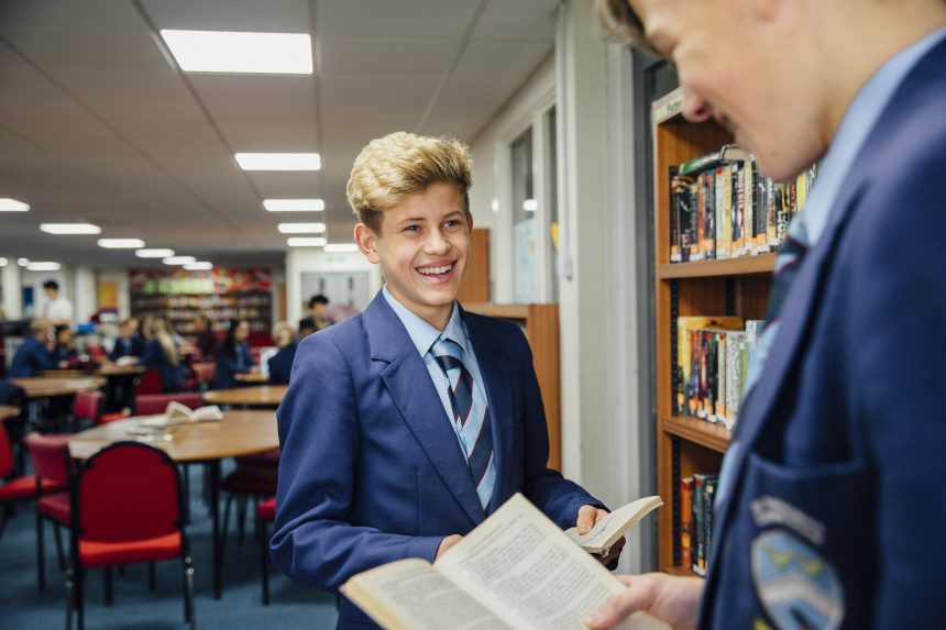 Two male teenagers reading together and smiling.