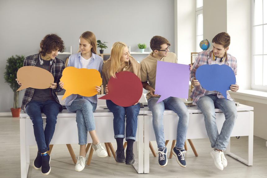 Five people sat on a desk holding speech bubbles.