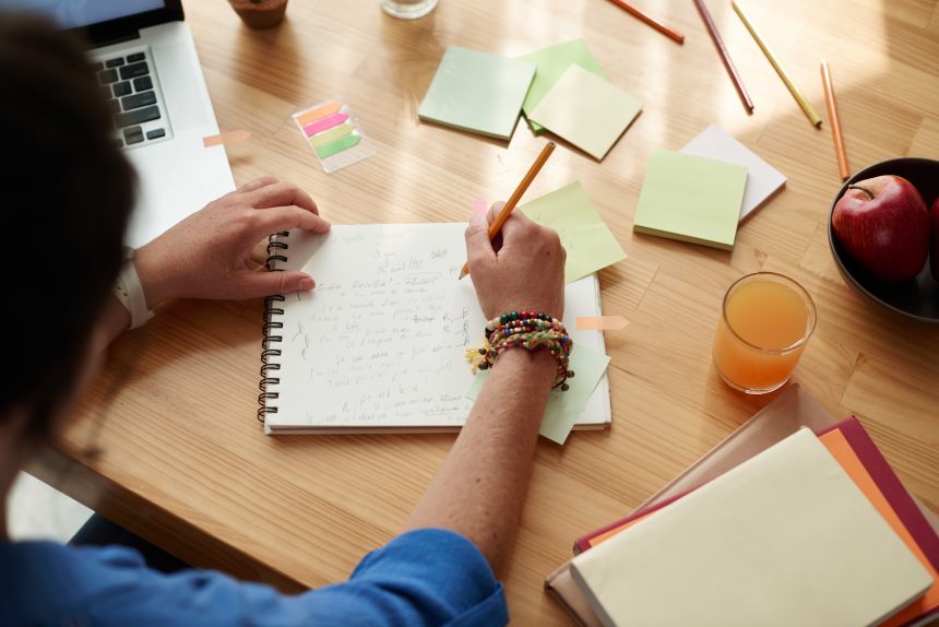 A student writing in a notebook and on sticky notes at their desk.