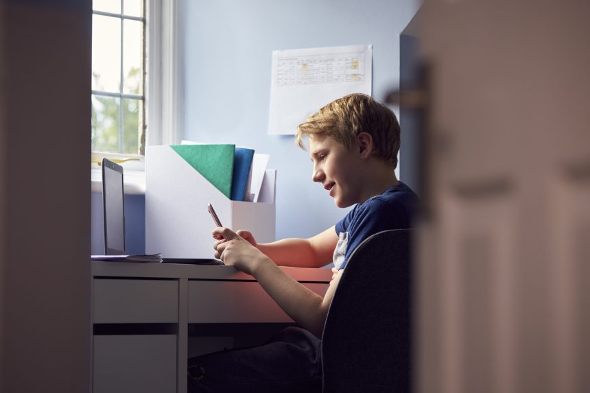 Teenage boy looking at his phone instead of his homework.