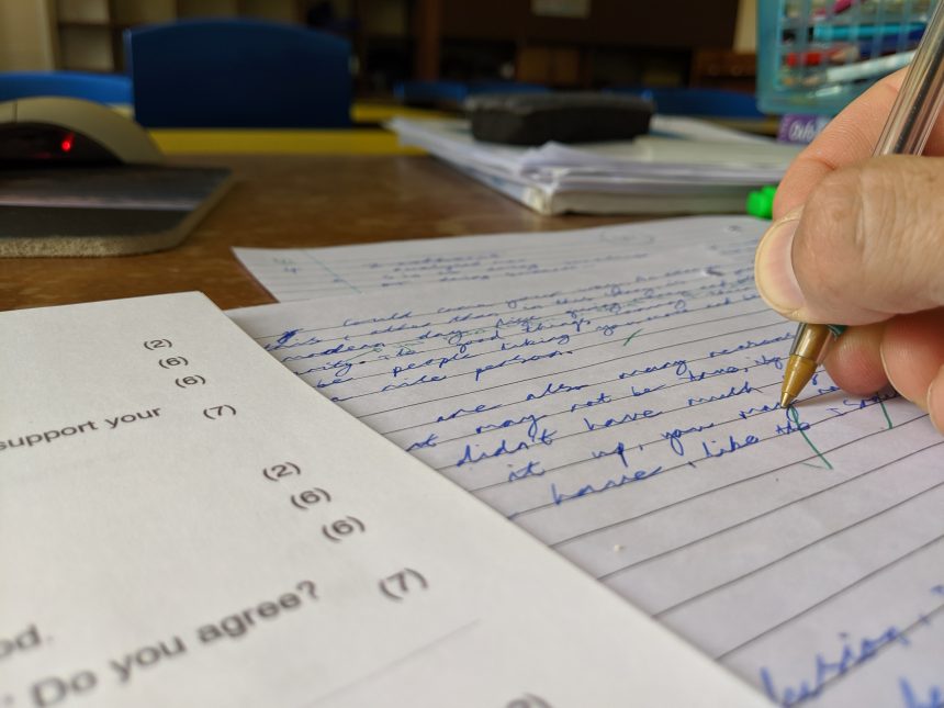 A teacher using a green pen to mark an essay.