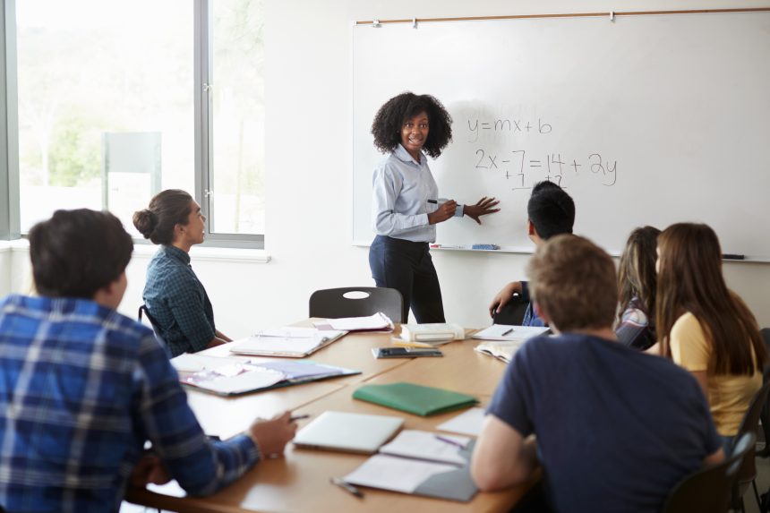 A female secondary school teacher teaching algebra on a whiteboard.