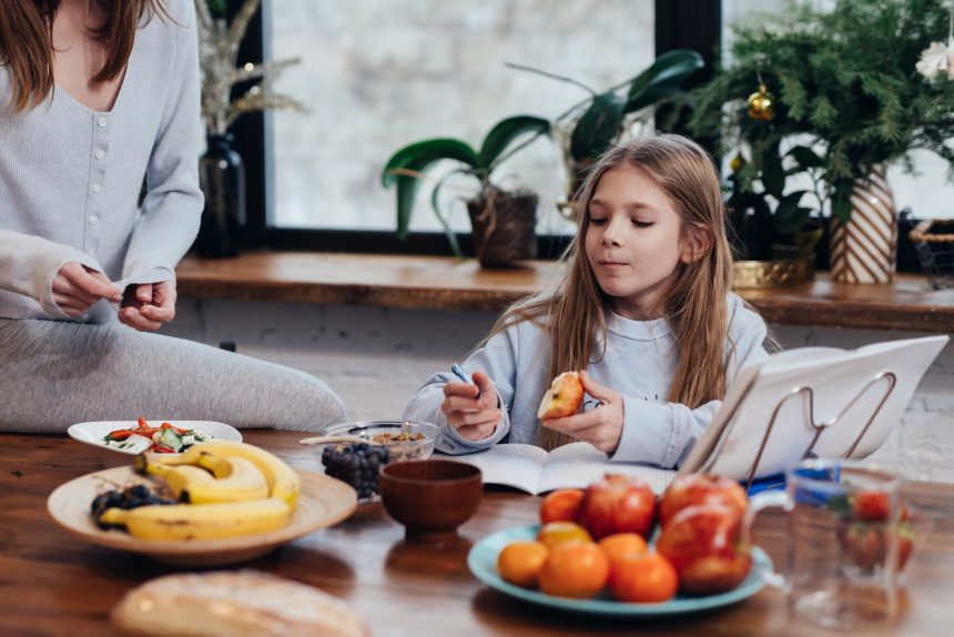 Young girl doing homework while her mother cooks dinner.