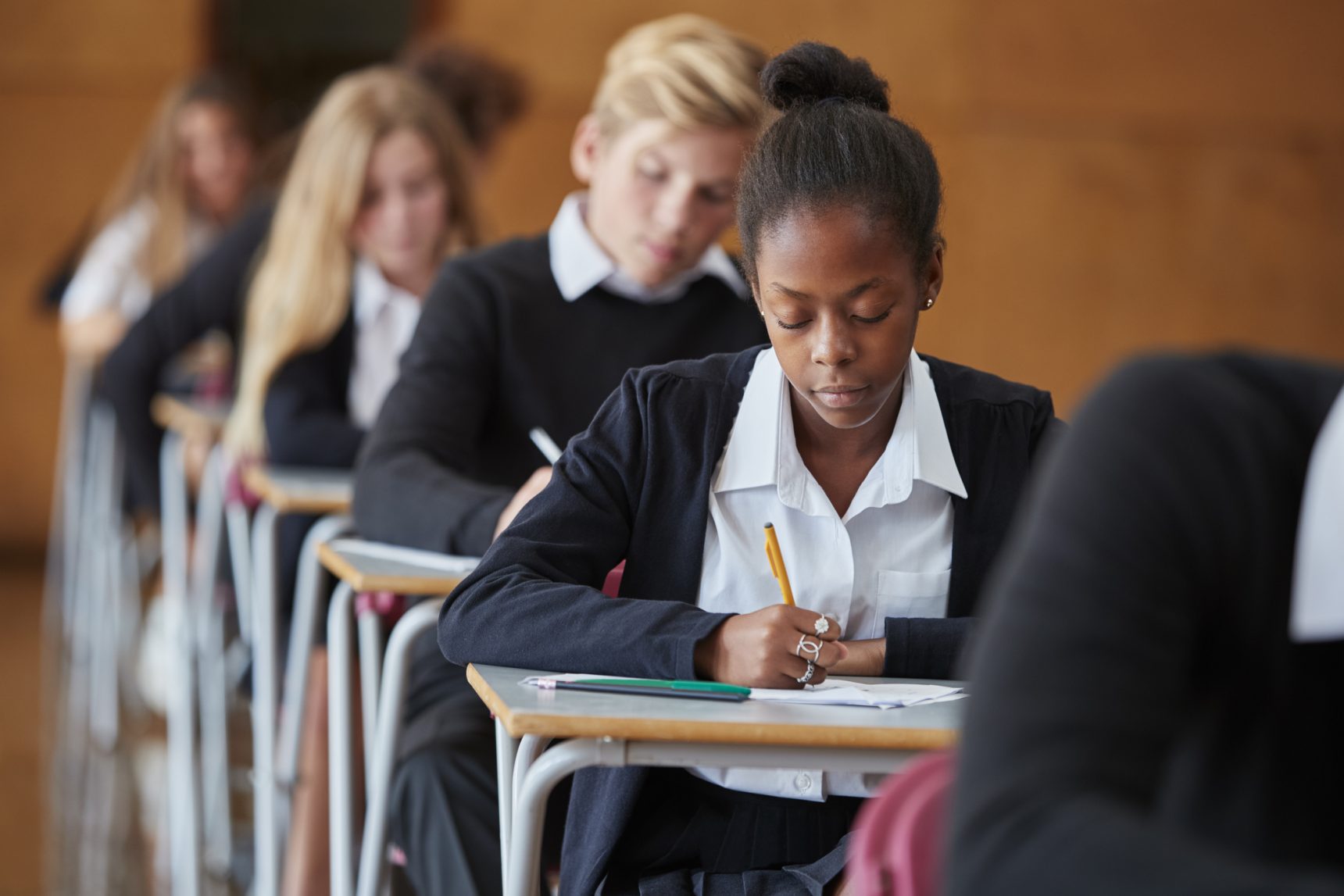 Students in uniform sitting an exam in the school hall.