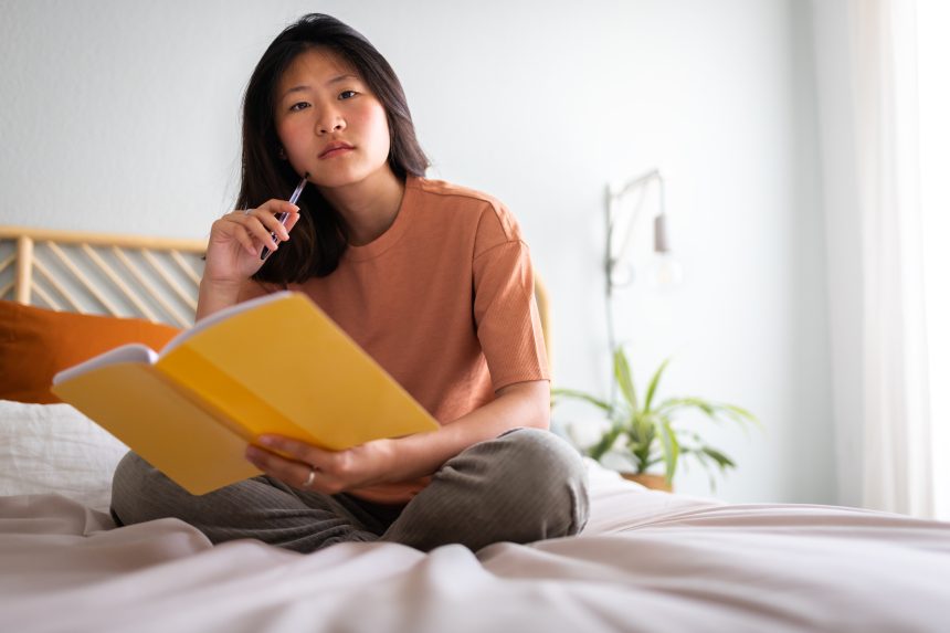 Female student sitting on bed revising and recalling information from memory.