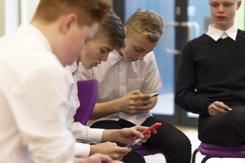 Three boys using smartphones in school.