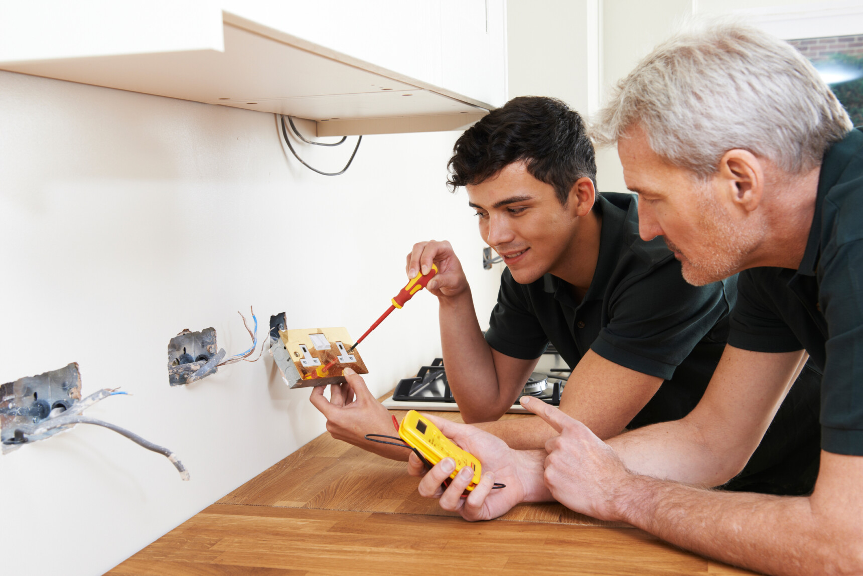 A young male apprentice working alongside an electrician.
