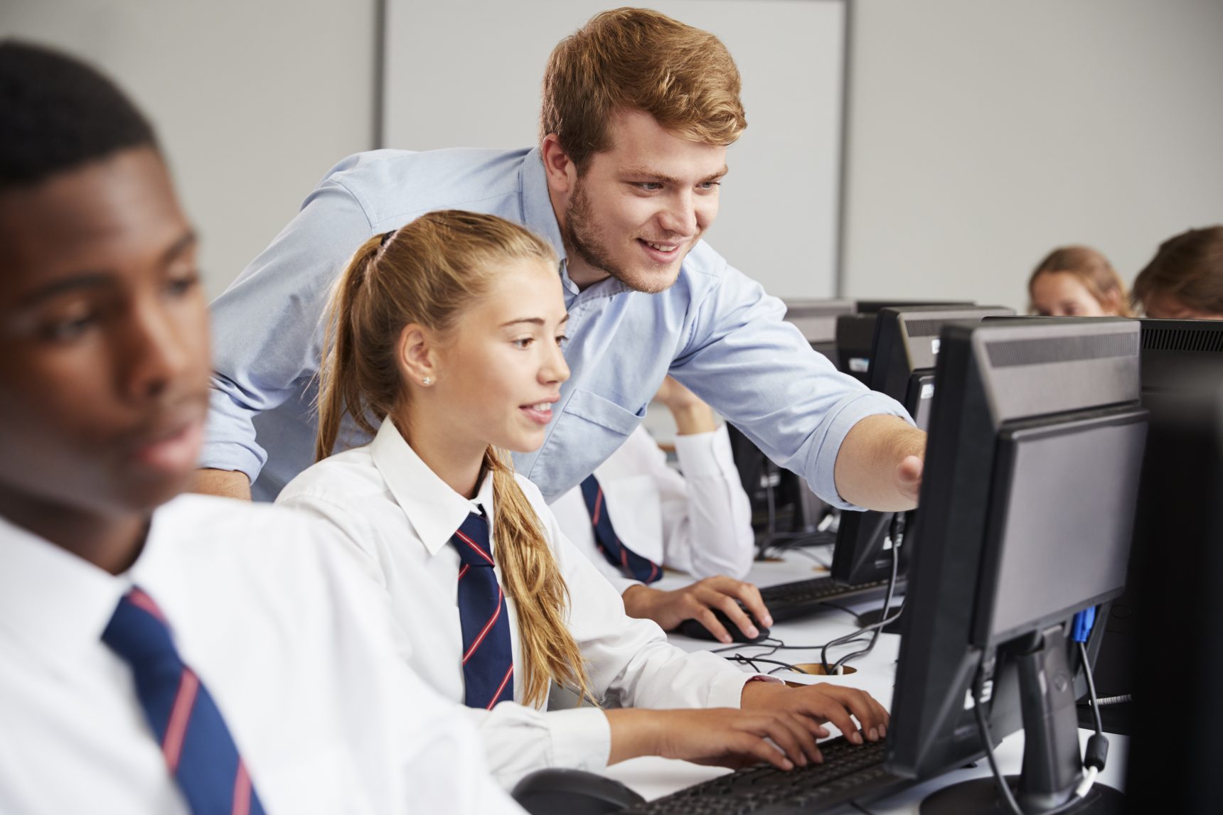 Smiling teacher helping his student in computer science class.