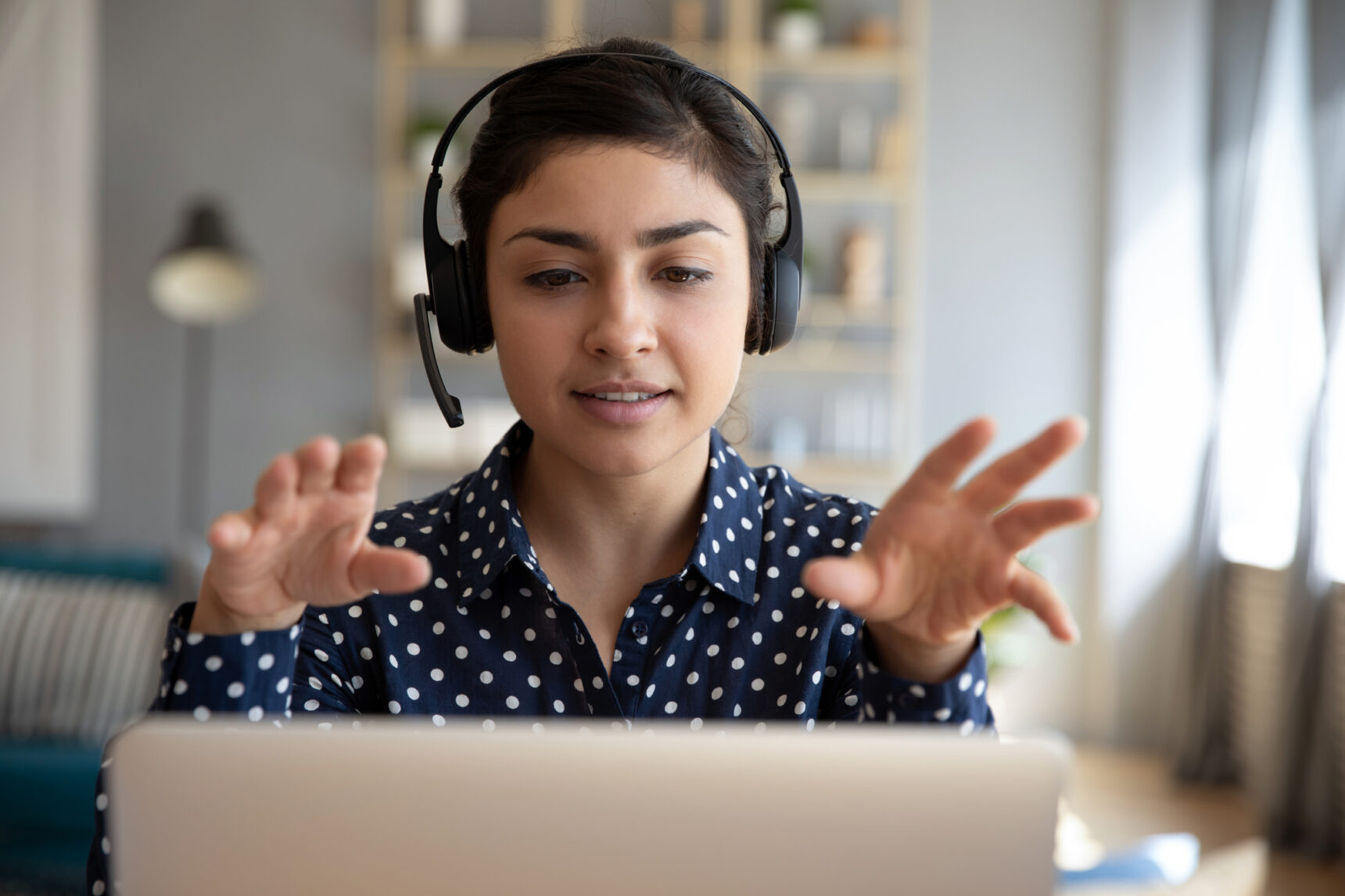 A femlae online tutor wearing a headset sits in front of her laptop giving a lesson to a student.