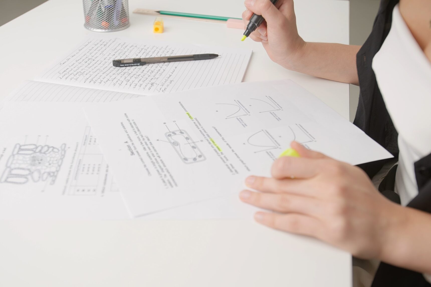 A student is revising at a desk, highlighting key terms on a biology past paper.