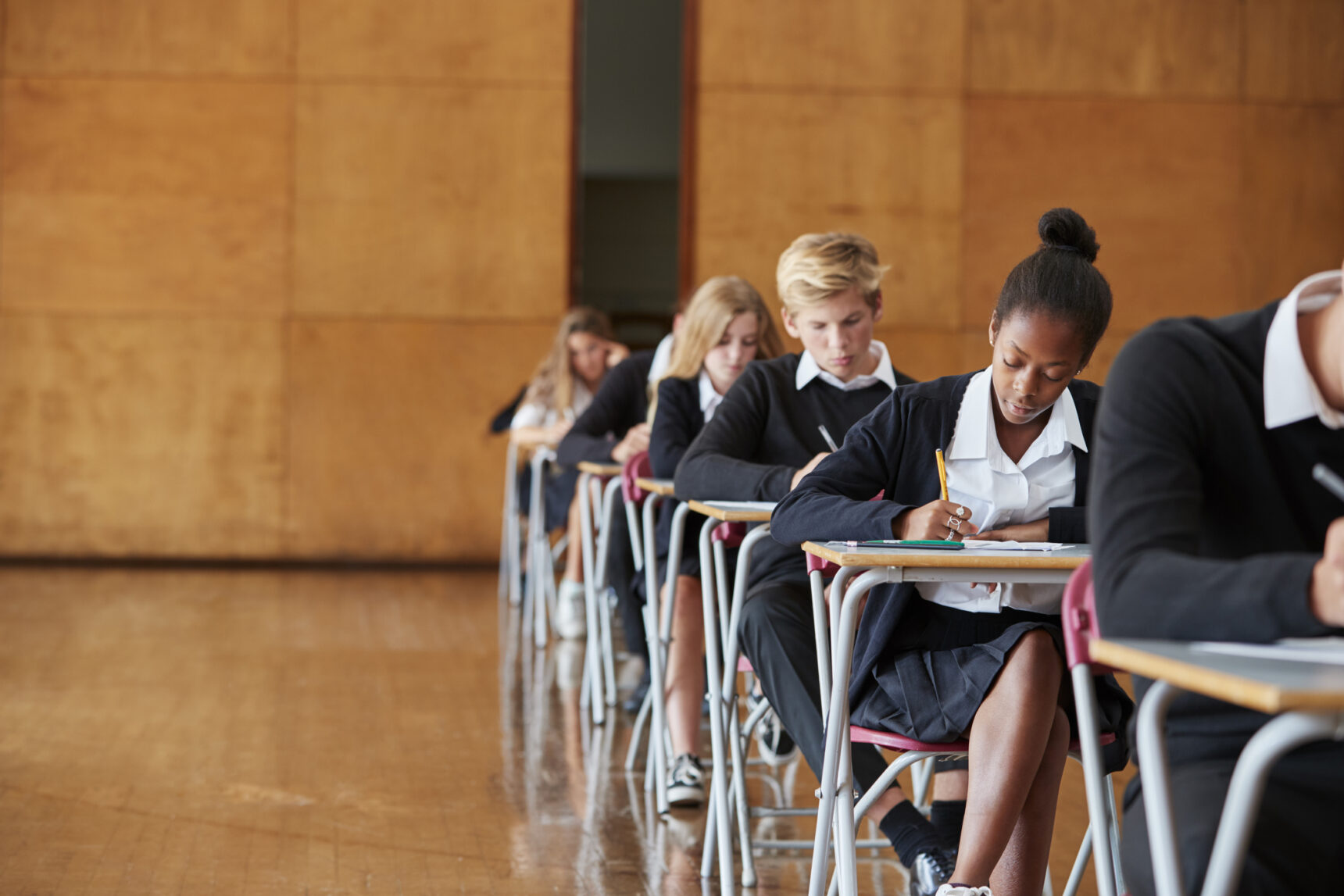 GCSE students are sitting the Geography Paper 3 exam in an exam hall.