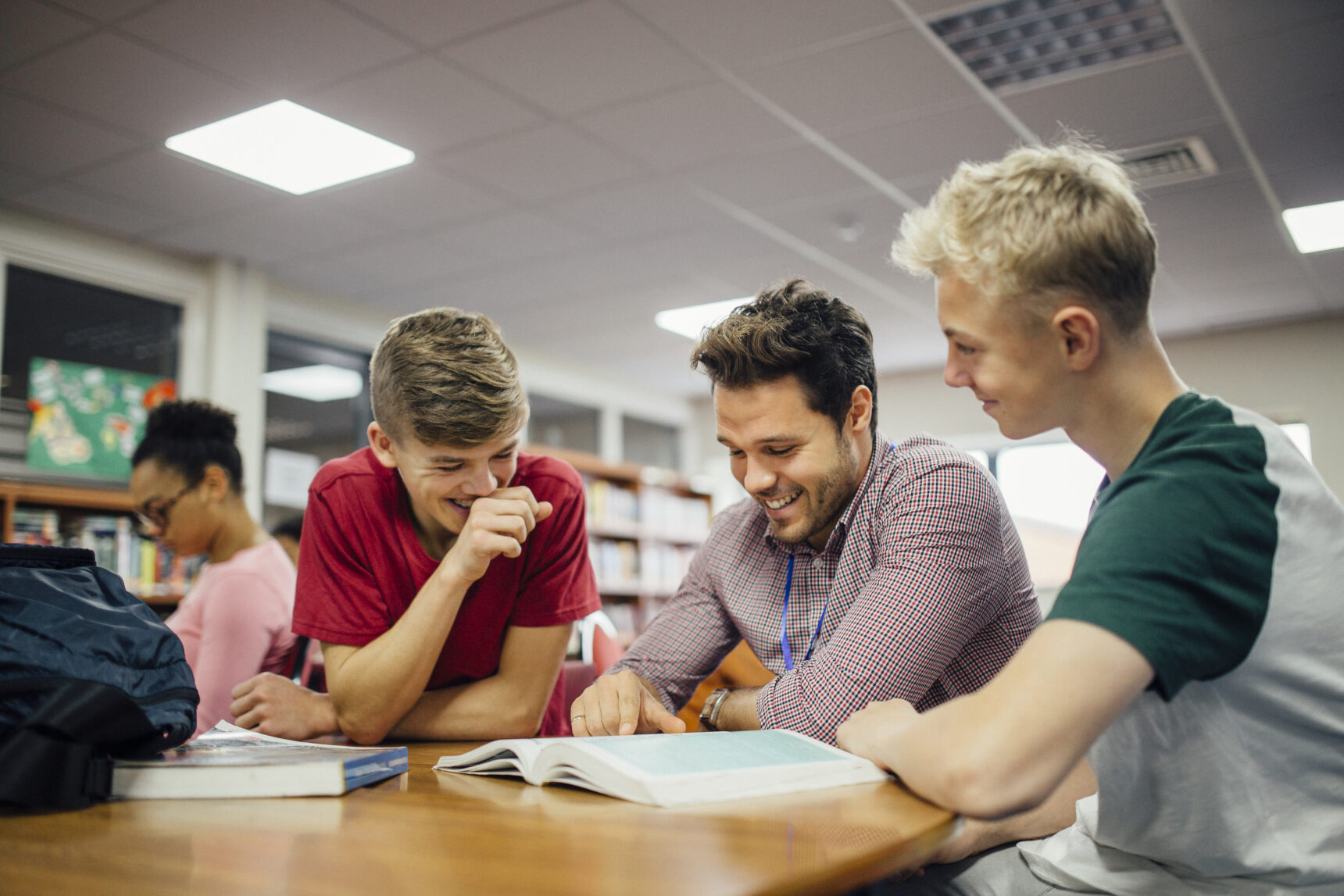 Male teacher laughing with two boys in school library.