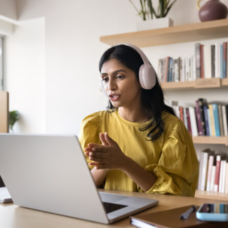A female tutor wearing a headset is talking to a student during an online tutoring session.