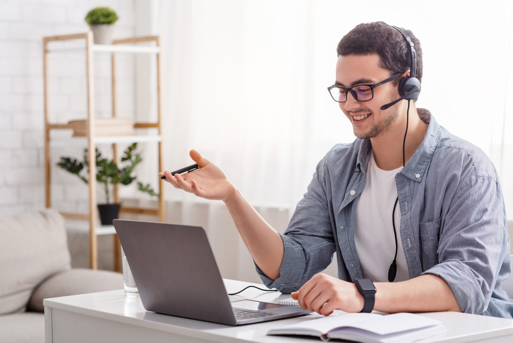 A male online tutor wearing a headset smiles as he talks to a student during an online tutoring maths lesson.