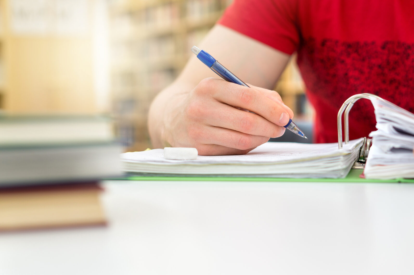 An A Level Pyschology student is writing notes as they sit at a desk surrounded by books.