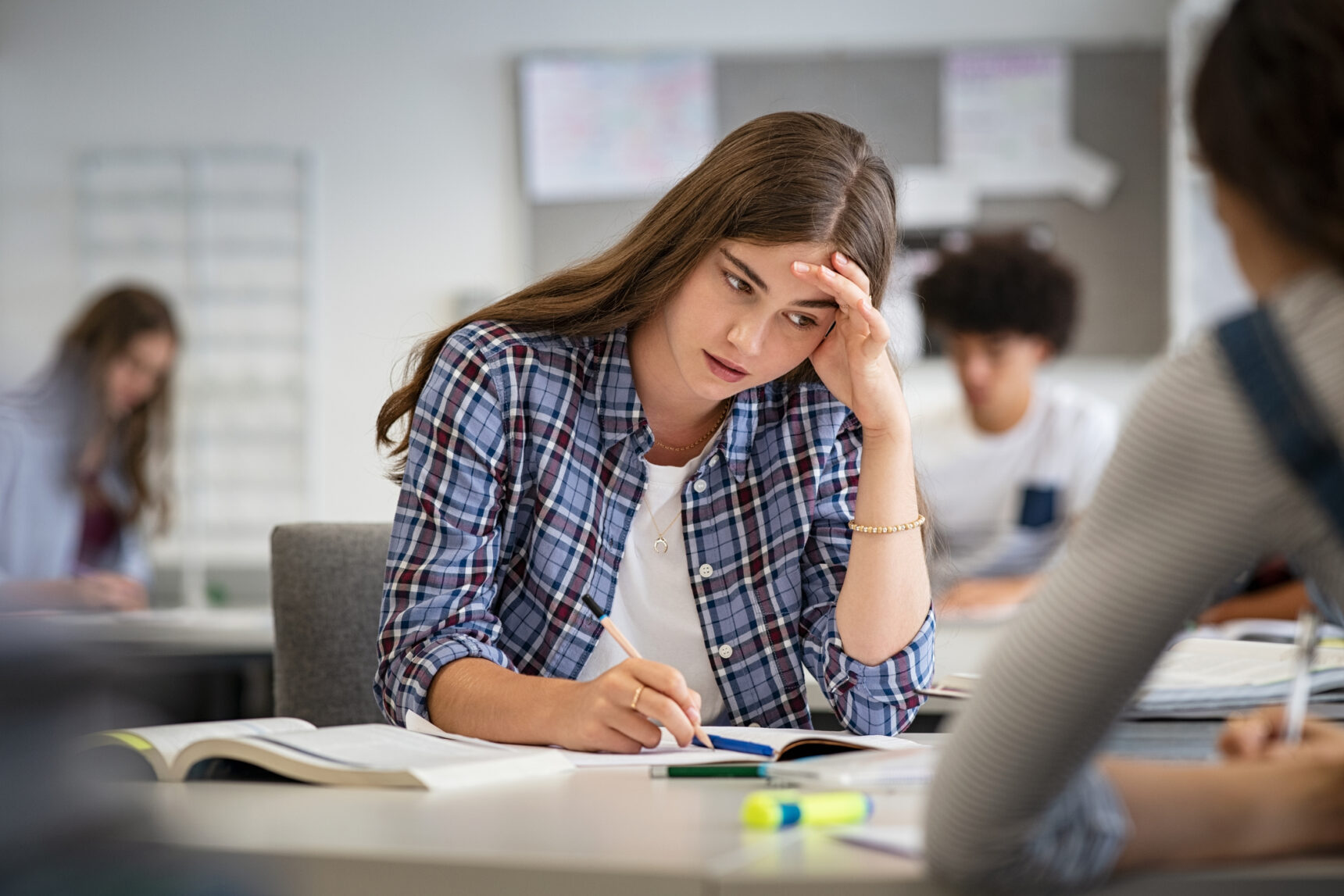 An anxoius student student with PDA is covering her face with her hand as she sits at a classroom desk.