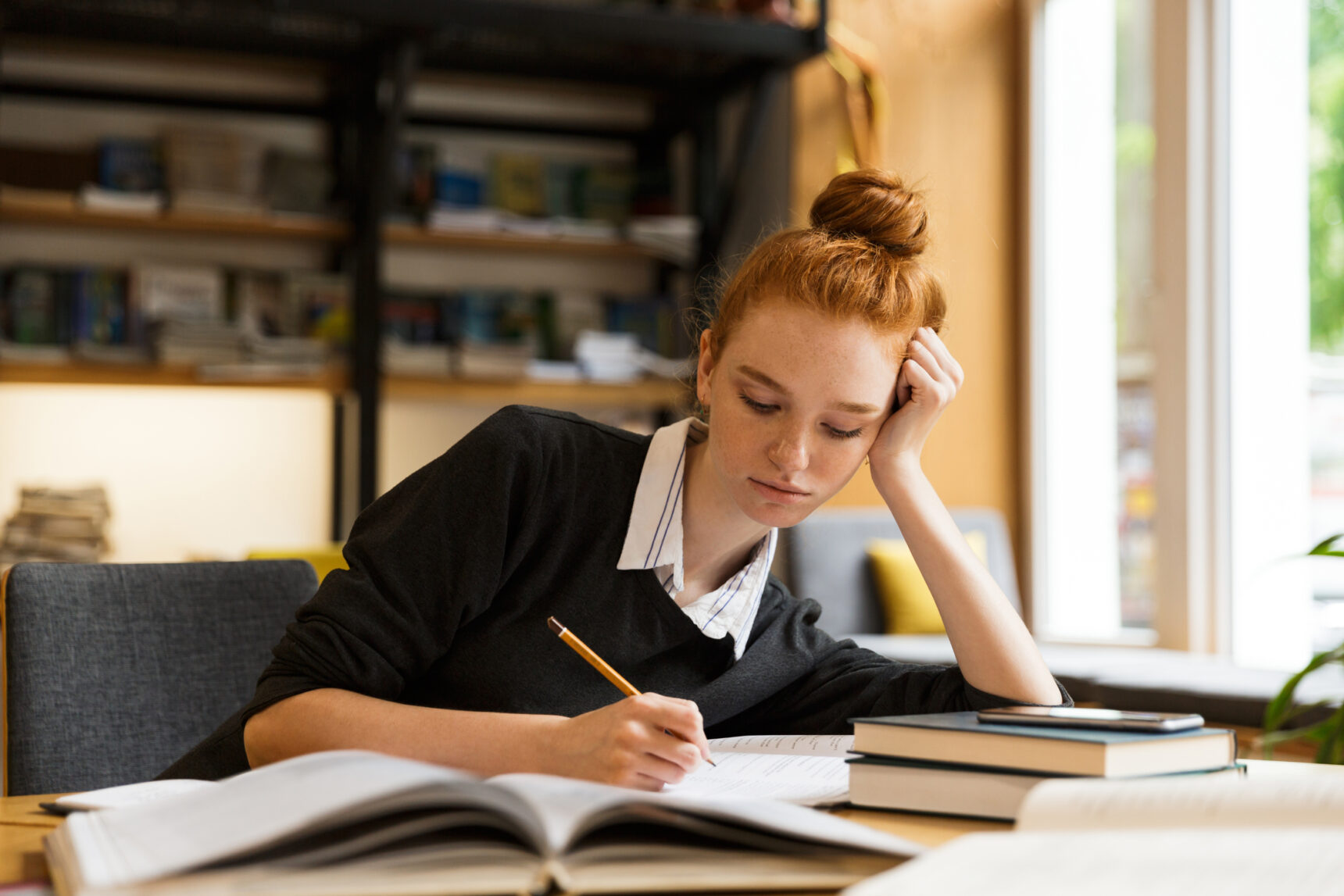 A GCSE student sits at a desk taking notes as she revises for exams.