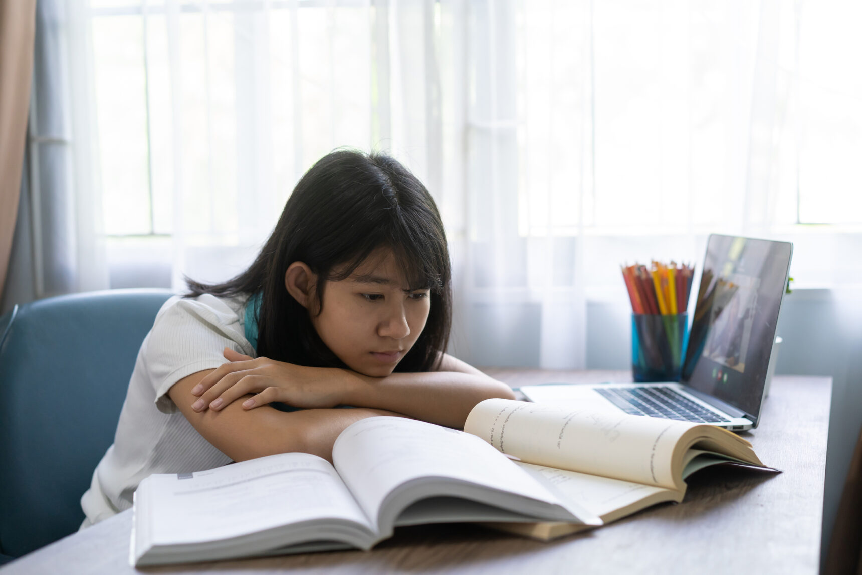 A young student rests her head on folded arms as she struggles with her homework.
