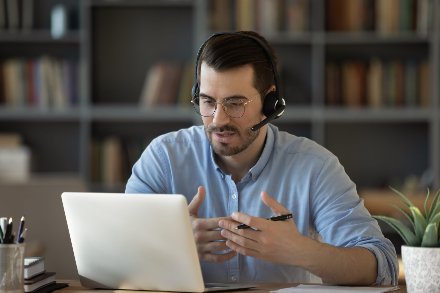 A male online tutor wearing a headset is delivering an online tutoring session via laptop.