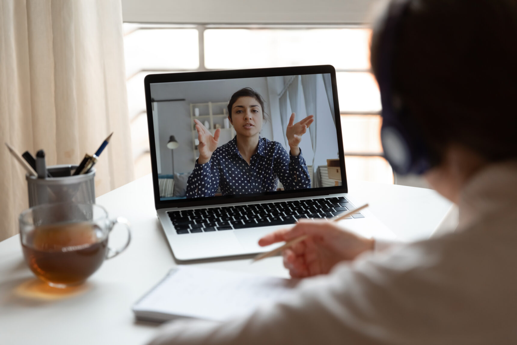 A student wearing a headset is listening and taking notes during an online tutoring session.
