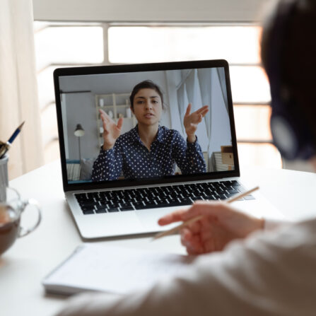 A student wearing a headset is listening and taking notes during an online tutoring session.