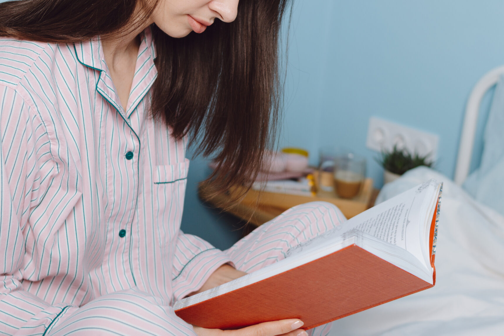 A teenage girl wearing pyjamas is reading a book before bed.