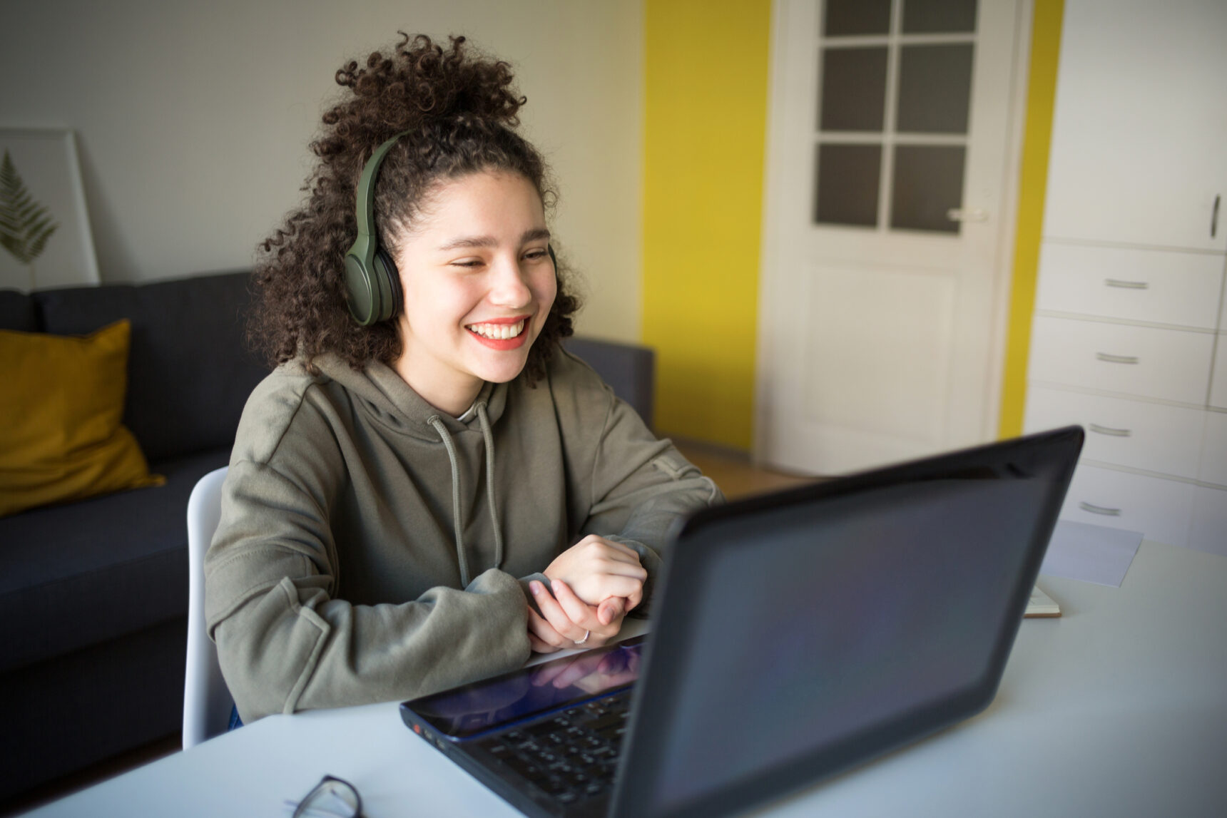 A teenage girl wearing earphones is smiling as she takes part in her first lesson with an online tutor.