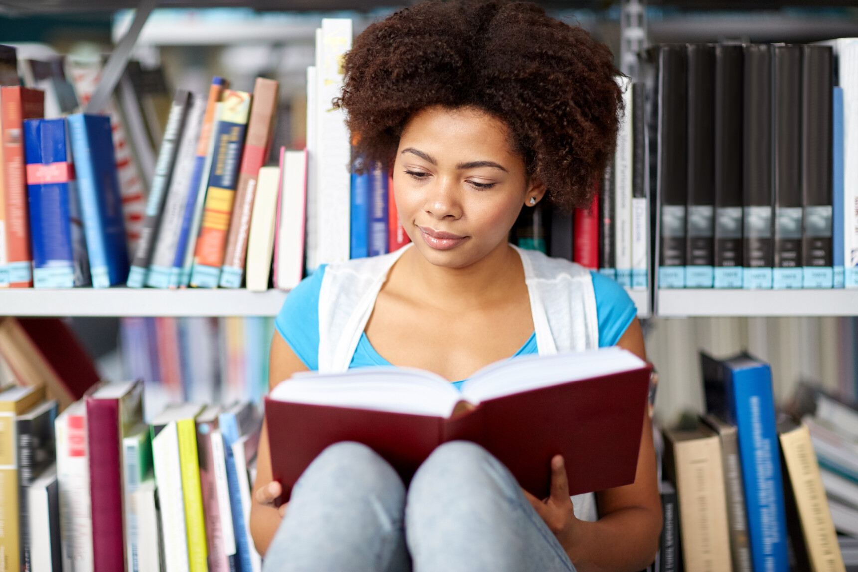 A female English tutor is sitting in the library reading a set text for GCSE English Literature.