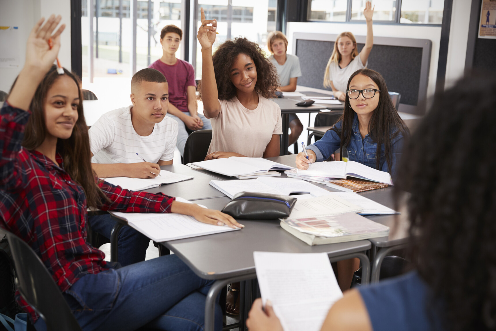 A group of students raise their hands to answer the teacher's question as part of formative assessment in the classroom.