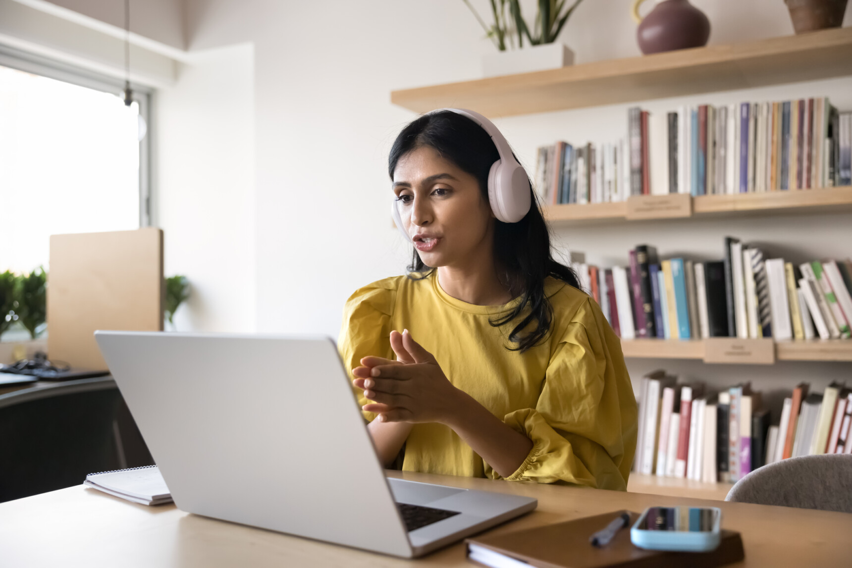 A female online tutor wearing a headset is speaking to a parent after delivering an online tutoring session.