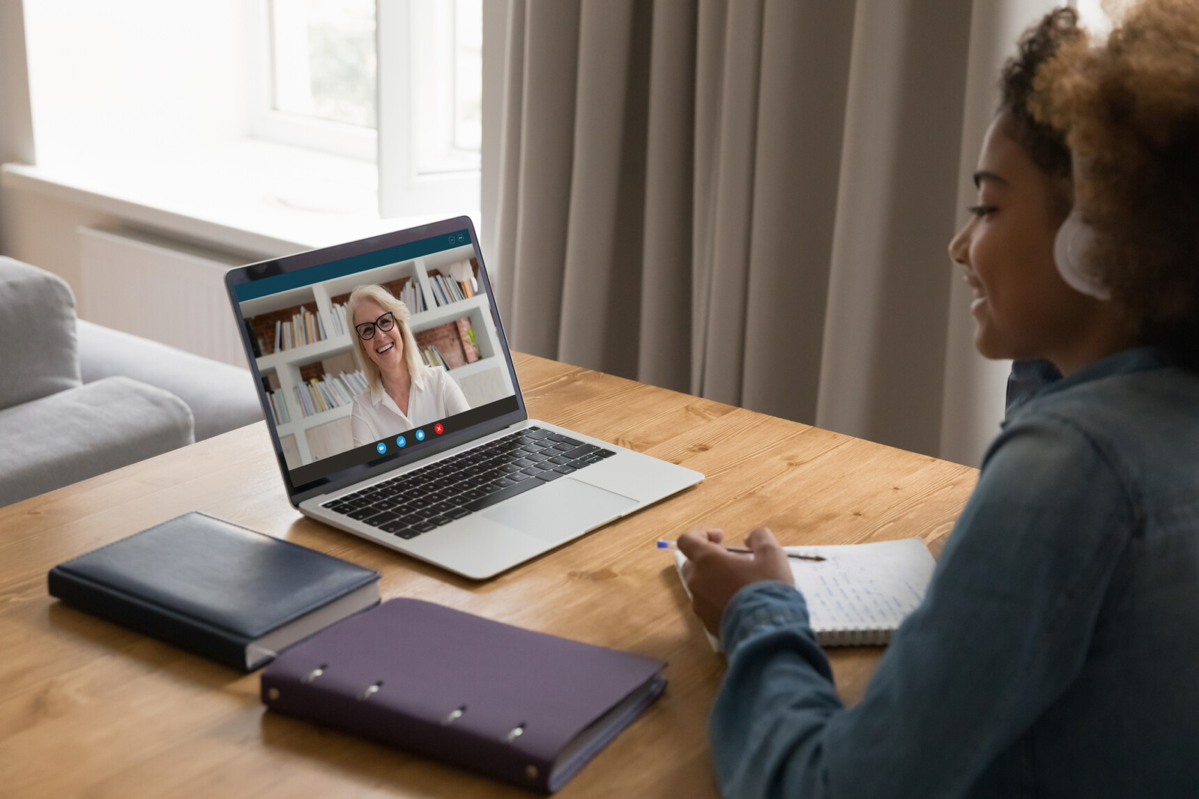 An student is smiling and taking notes during an online tutoring session.