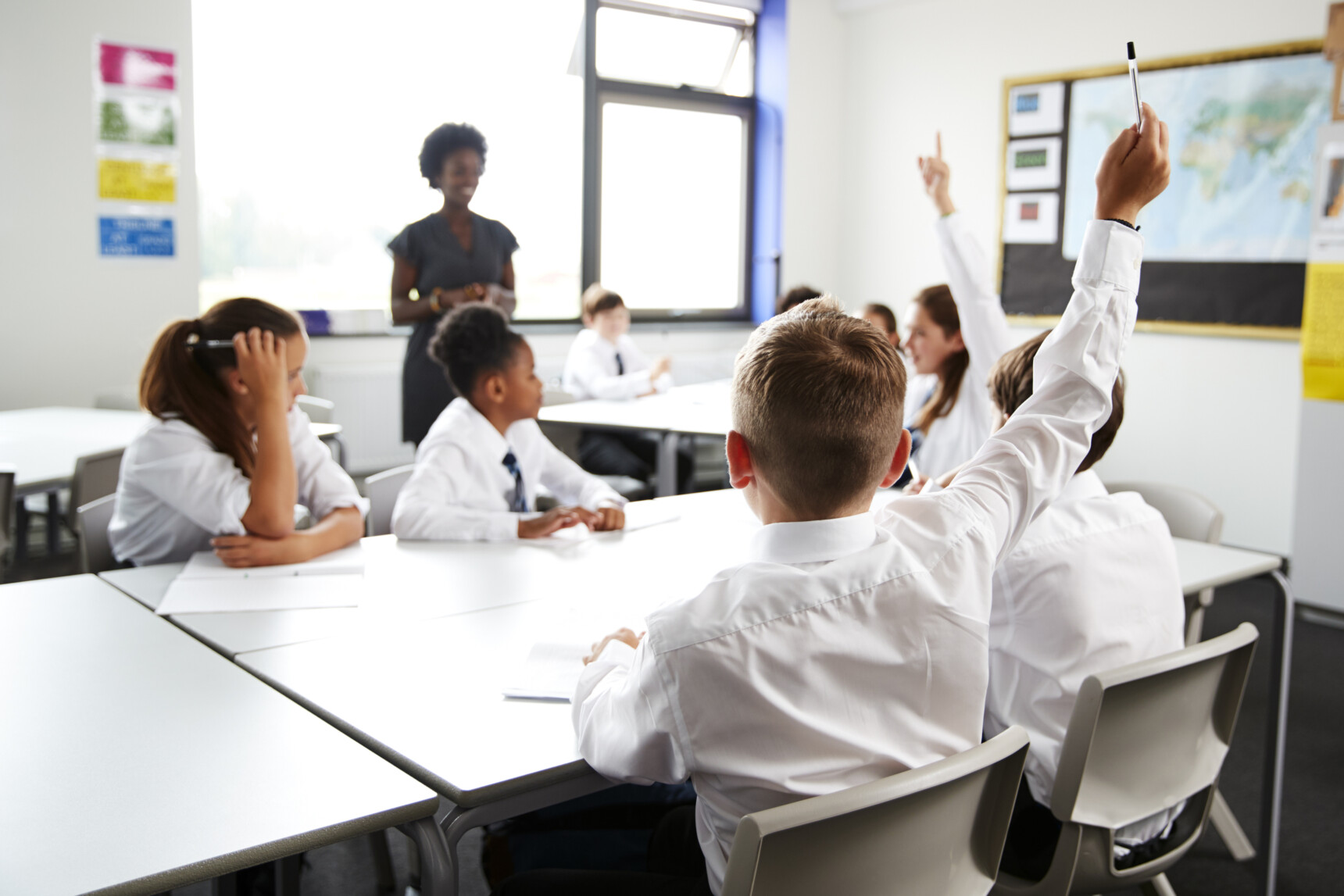 Students raise their hands during a classroom lesson as their teacher leads the discussion, representing equality and equity through inclusive participation and learning opportunities.