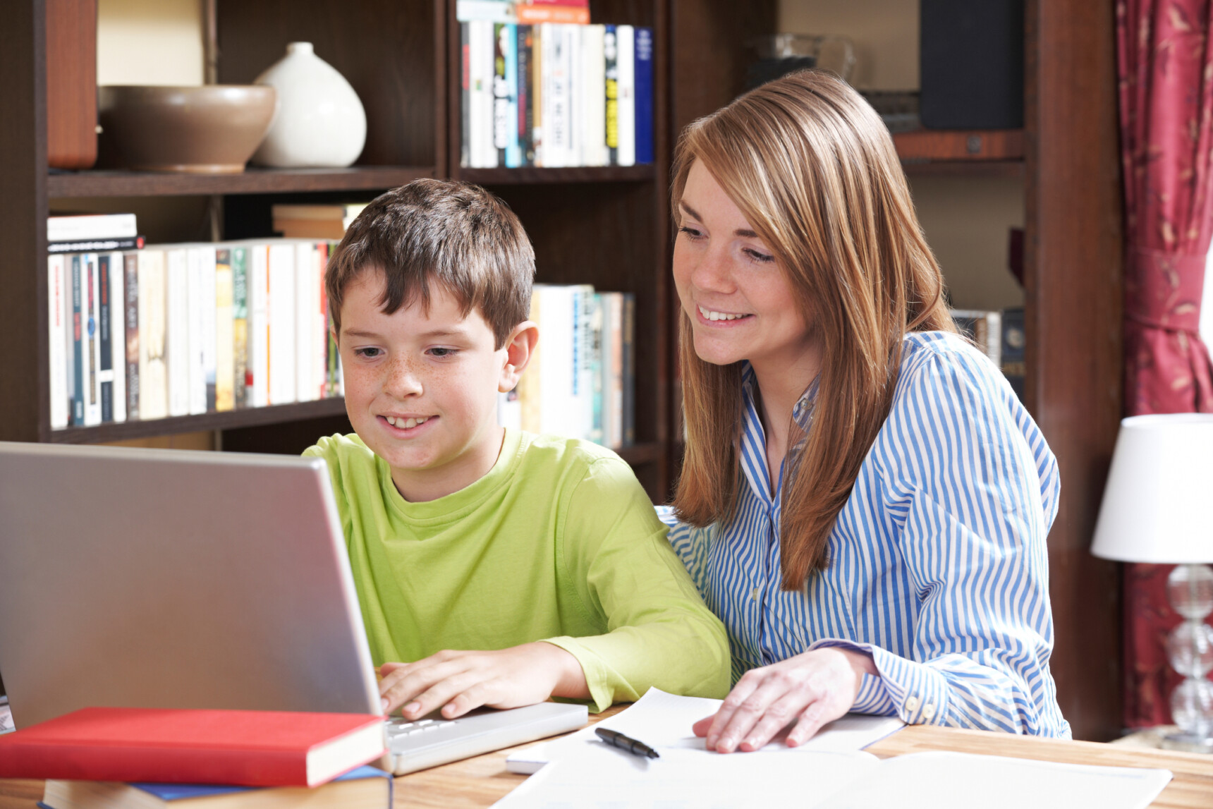A mother is supporting her son with online learing on a laptop as part of his home education.