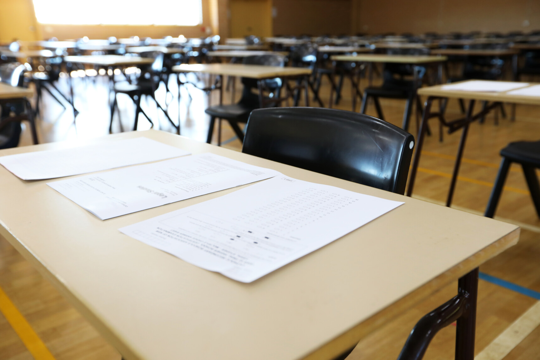 Empty A Level exam hall with exam papers laid out on desks.