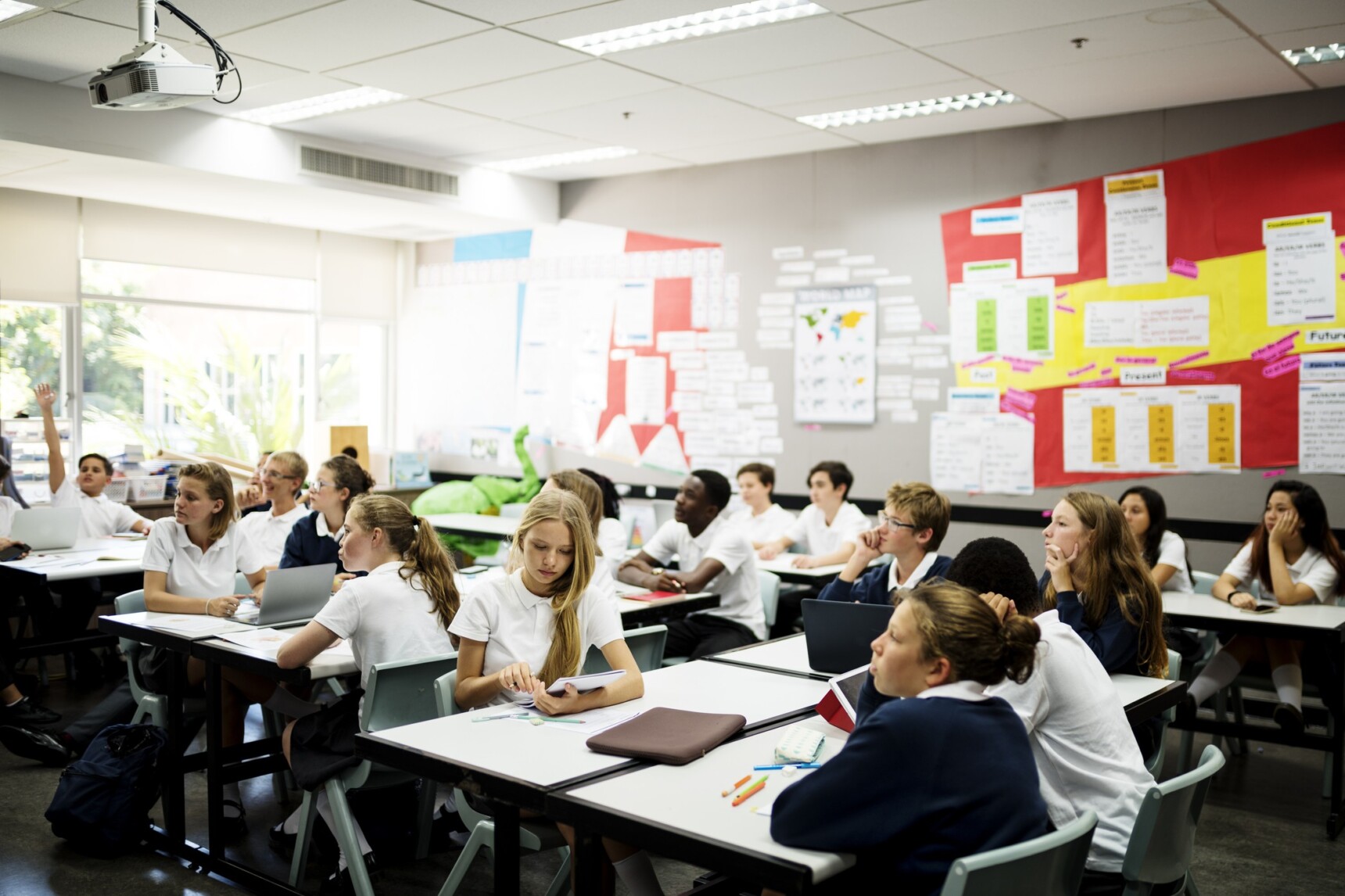 Pupils looking towards the front of the classroom during a lesson, with one pupil raising their hand to answer a question.